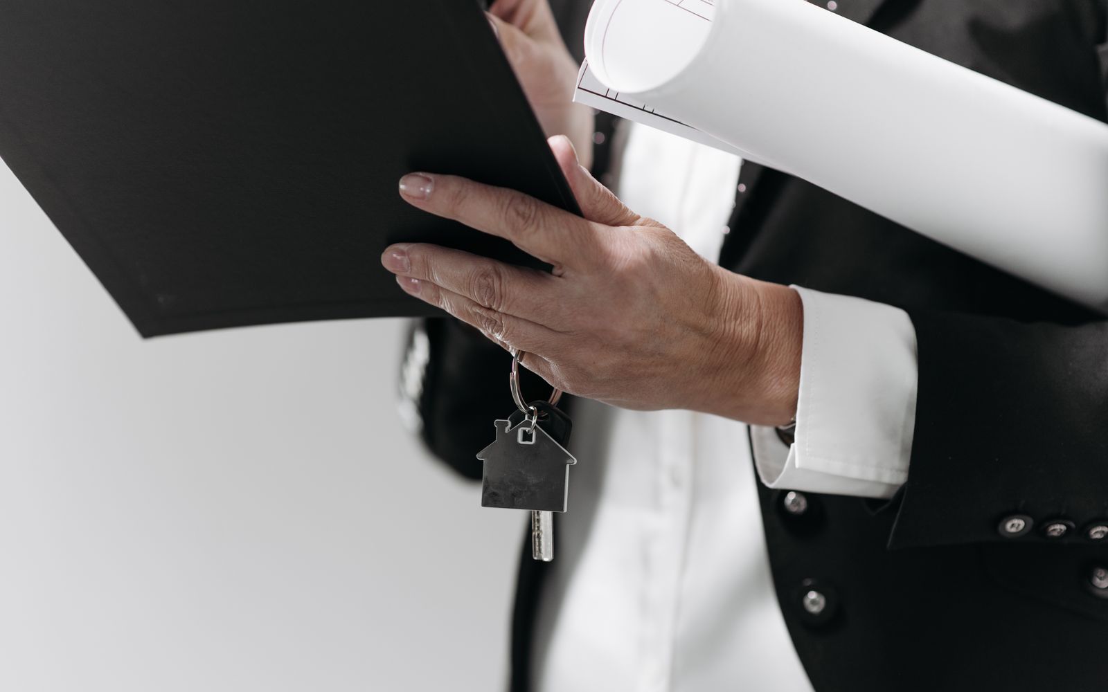 Close-up of a business professional holding a house key and architectural plans, symbolizing real estate.