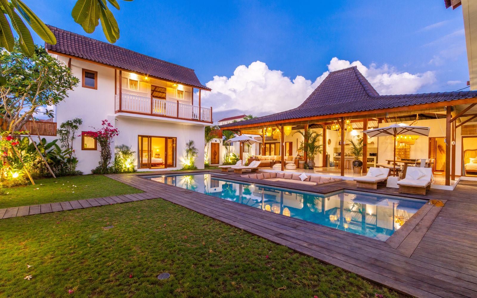 Tropical villa exterior with a pool, wooden deck and garden under a blue sky