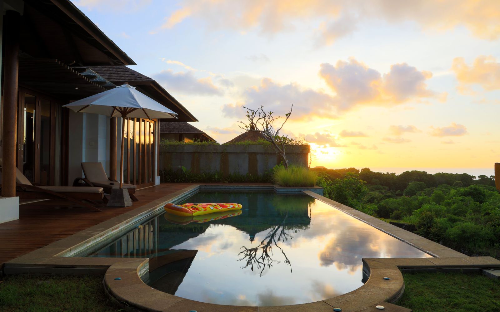 A serene view of a villa's infinity pool at sunset in Bali, Indonesia, with lush greenery and calm reflections.