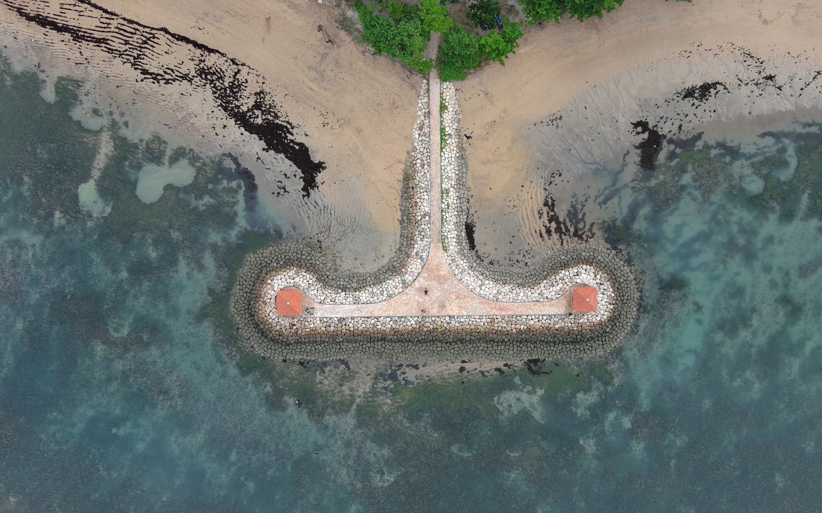 Drone shot capturing the unique stone pier and coastline of Sanur with turquoise waters.